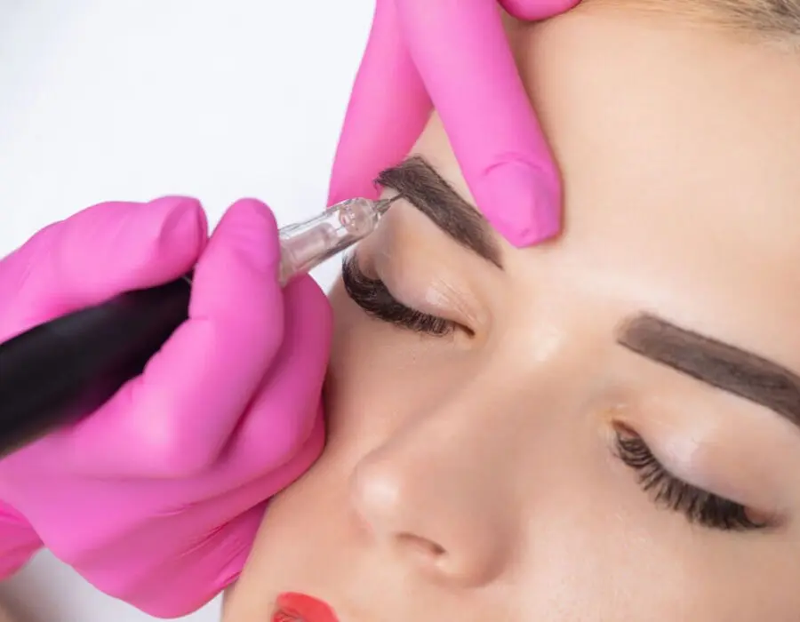 Close-up of a permanent makeup procedure on eyebrows with pink gloves