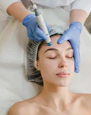Relaxed woman receiving a facial treatment with a head wrap and blue towels